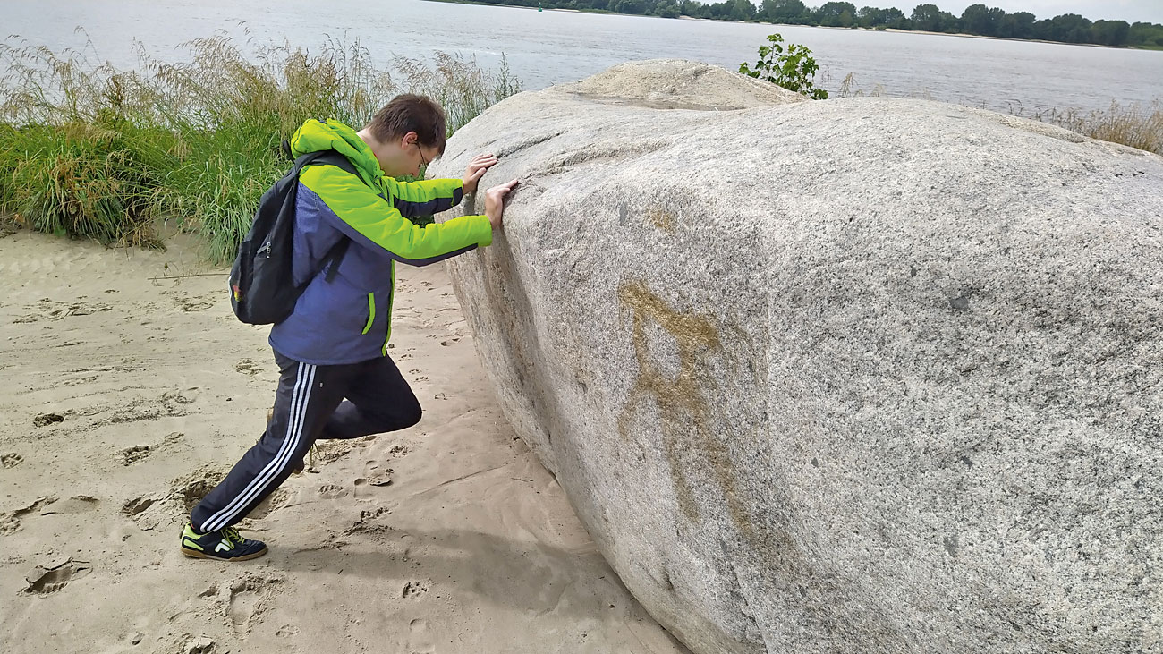 Ein Beschäftigen des LHW versucht, einen großen Stein, der am Elbstrand liegt, wegzuschieben.